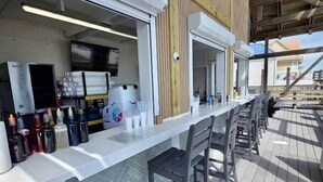 A bar area with a counter, stools, and a view of the outside. - Steps to Pvt beach/Beach ramp/2 pools/Sleeps 18 (Miramar Beach)