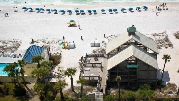 A beach with umbrellas, a pool, and a building with a green roof. - Steps to Pvt beach/Beach ramp/2 pools/Sleeps 18 (Miramar Beach)