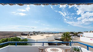 A balcony with a table and chairs, overlooking a coastal town with white buildings and a clear sky. - 3BR Home - Private Heated Pool - Parking (Playa Blanca)