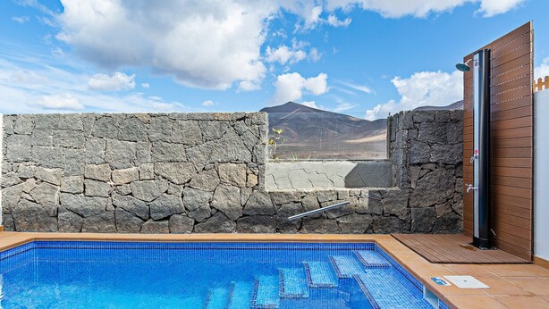 A swimming pool with a stone wall and a wooden door, set against a mountainous backdrop. - 3BR Home - Private Heated Pool - Parking (Playa Blanca)