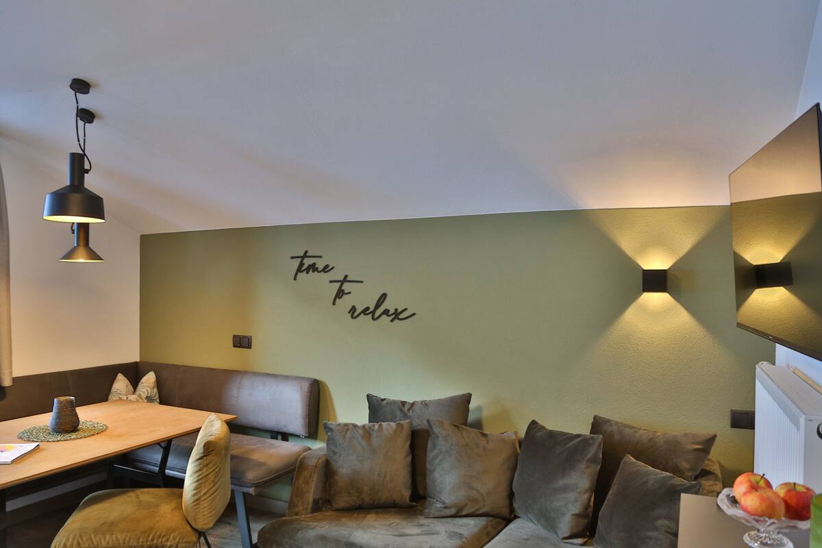Um quarto acolhedor com uma mesa de madeira, assentos acolchoados e uma parede com uma frase motivacional.