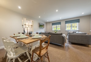 A dining area with a wooden table set for four, a grey sofa, and a grey couch in a living room.