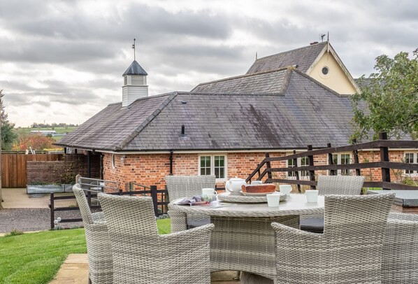 A brick house with a sloped roof and a chimney. There is a patio with wicker furniture and a table set for dining.