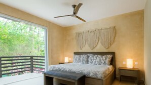 Une chambre à coucher avec un lit, deux tables de chevet, un ventilateur de plafond et une vue sur la verdure.