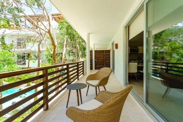 Un balcon avec des meubles en osier, une porte vitrée donnant sur une pièce et une vue sur une piscine.