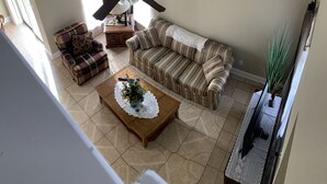 Een woonkamer met een bank, fauteuil, salontafel en plafondventilator.