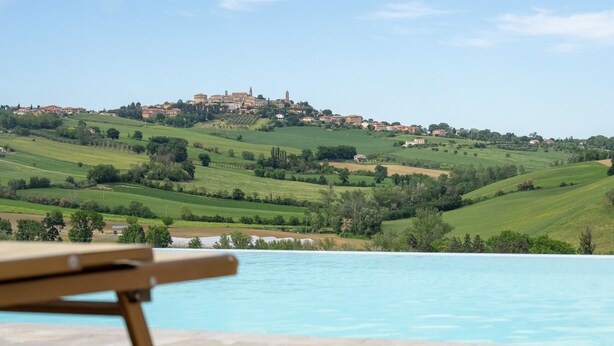 A poolside view with a chair, a view of rolling green hills, and a distant building. - Villa Edelia, Villa for exclusive use in Mondavio, Le Marche (Mondavio)