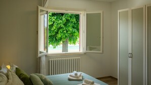 A bedroom with a bed, a window with a view of a tree, a radiator, and a wardrobe. - Villa Edelia, Villa for exclusive use in Mondavio, Le Marche (Mondavio)