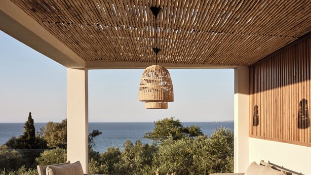 Un espacio de estar al aire libre cubierto con mobiliario de mimbre y una lámpara colgante, con vistas panorámicas al mar.
