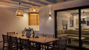 Un comedor moderno con una mesa de madera y sillas de mimbre, un jarrón grande con flores y lámparas colgantes de mimbre.