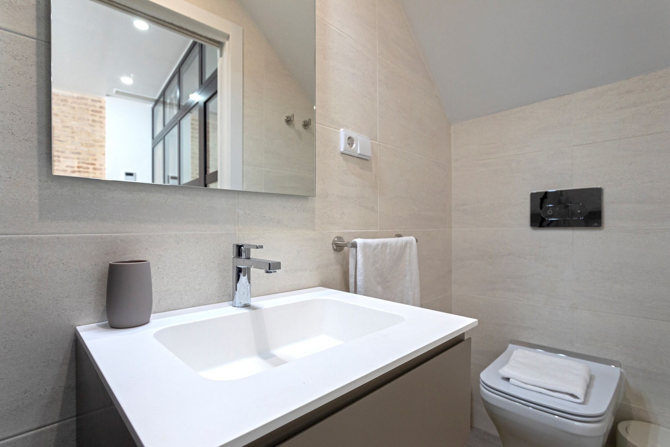 A modern bathroom with a white sink, a mirror, a towel rack, and a toilet.