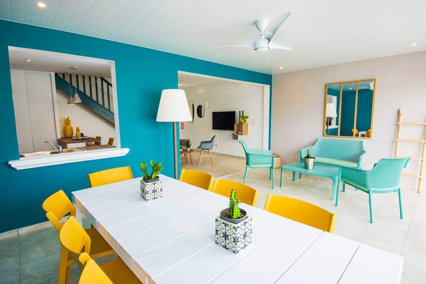 A modern living room with a white dining table, yellow chairs, and teal sofas.