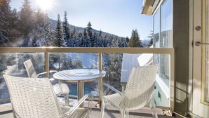 En balkon med gelænder af glas, et rundt bord og fire fletstole.