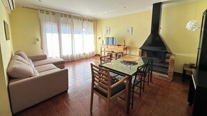Ein Wohnzimmer mit einer Couch, einem Glastisch, Stühlen, einem Fernseher und einem Kamin.