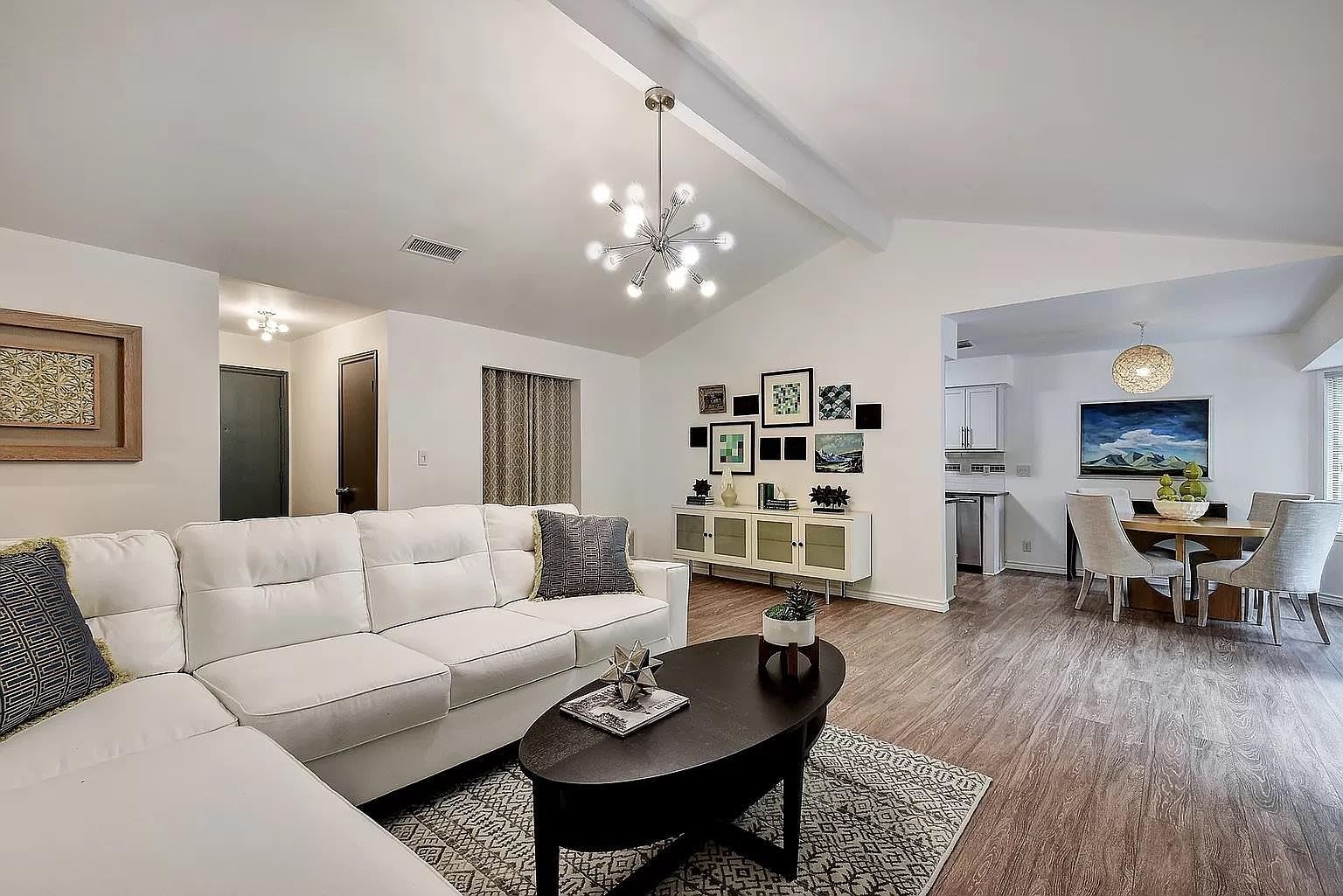 A modern living room with a white sofa, a coffee table, and a dining area with a table and chairs.
