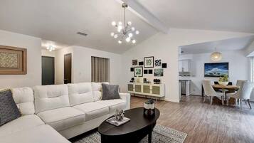 A modern living room with a white sofa, a coffee table, and a dining area with a table and chairs.
