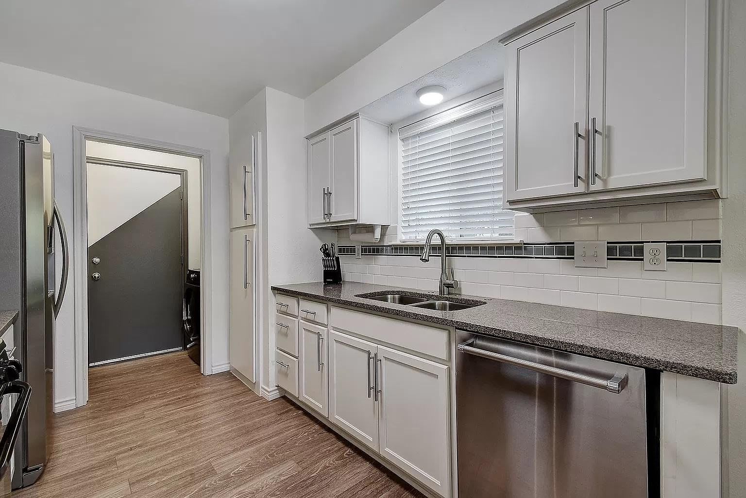 A modern kitchen with white cabinetry, a granite countertop, and a stainless steel sink.