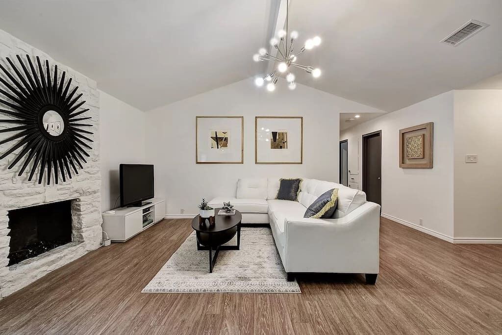 A modern living room with a fireplace, white sofa, black coffee table, and framed pictures on the wall.