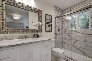 A bathroom with a marble vanity, a large mirror with a geometric frame, a toilet, and a shower with a glass door.