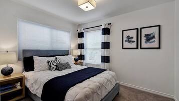 A bedroom with a bed, bedside tables, a lamp, a window with blinds, and two framed pictures on the wall.