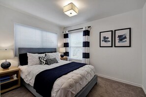 A bedroom with a bed, bedside tables, a lamp, a window with blinds, and two framed pictures on the wall. - Stylish 3BR | King Bed | ACL x Formula 1 (Austin)