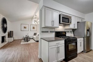 A modern kitchen with white cabinetry, a stainless steel refrigerator, a microwave, and a stove. - Stylish 3BR | King Bed | ACL x Formula 1 (Austin)