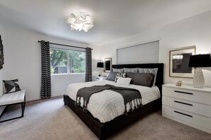 A modern bedroom with a large bed, bedside tables, a dresser, and a window with curtains.