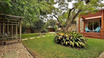 A well-maintained backyard with a wooden pergola, a seating area with chairs, and a stone building with a glass door.