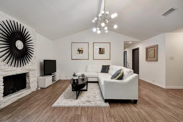 A modern living room with a fireplace, a white sofa, a coffee table, and artwork on the walls.
