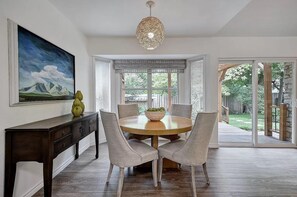 A dining area with a round table, chairs, a chandelier, and a painting on the wall.