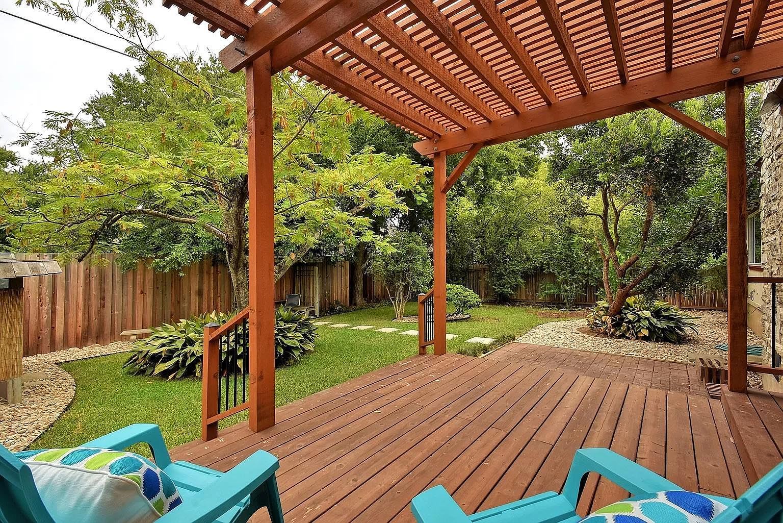 A wooden deck with a pergola, surrounded by a grassy yard and trees.