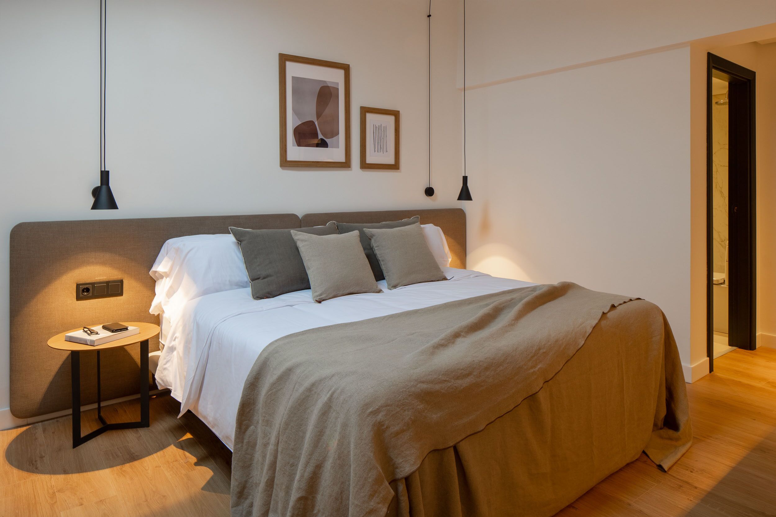 A modern bedroom with a large bed, a bedside table, and two pendant lights.