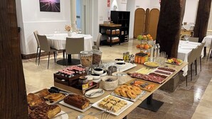 A buffet setup with various food items, including pastries, meats, and condiments, arranged on a long table in a well-lit room with a tiled floor and modern decor. - EtxeAundi Hotel Boutique (Oñati)