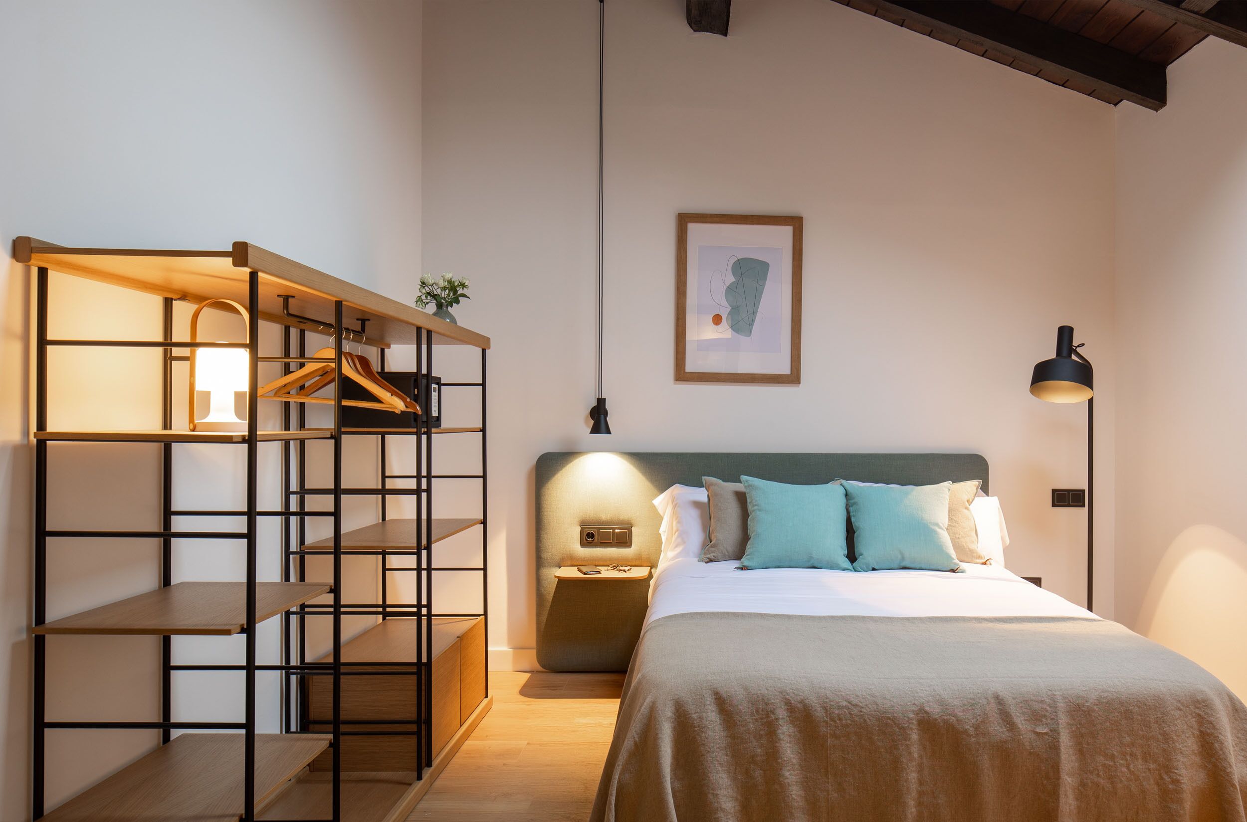 Un dormitorio con cama, mesitas de noche, un perchero y una obra de arte enmarcada en la pared.