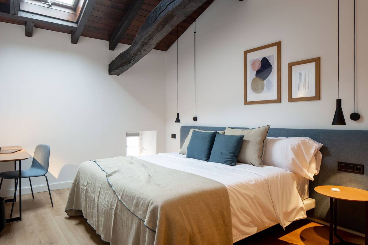 A bedroom with a bed, a desk, a chair, and a small table.
