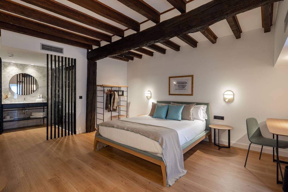 A bedroom with a wooden bed, a bedside table, a chair, and a bathroom with a mirror and sink.