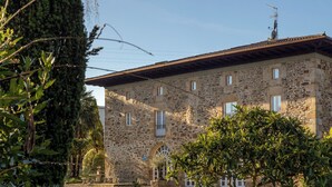 A stone building with a tiled roof, multiple windows, and a small garden area with a tree. - EtxeAundi Hotel Boutique (Oñati)