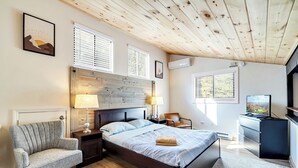 Een slaapkamer met een houten plafond, een bed met hoofdeinde, een nachtkastje, een stoel, een bureau en een televisie.