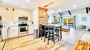 Een moderne keuken met witte kasten, roestvrijstalen apparatuur en een houten eettafel met stoelen.