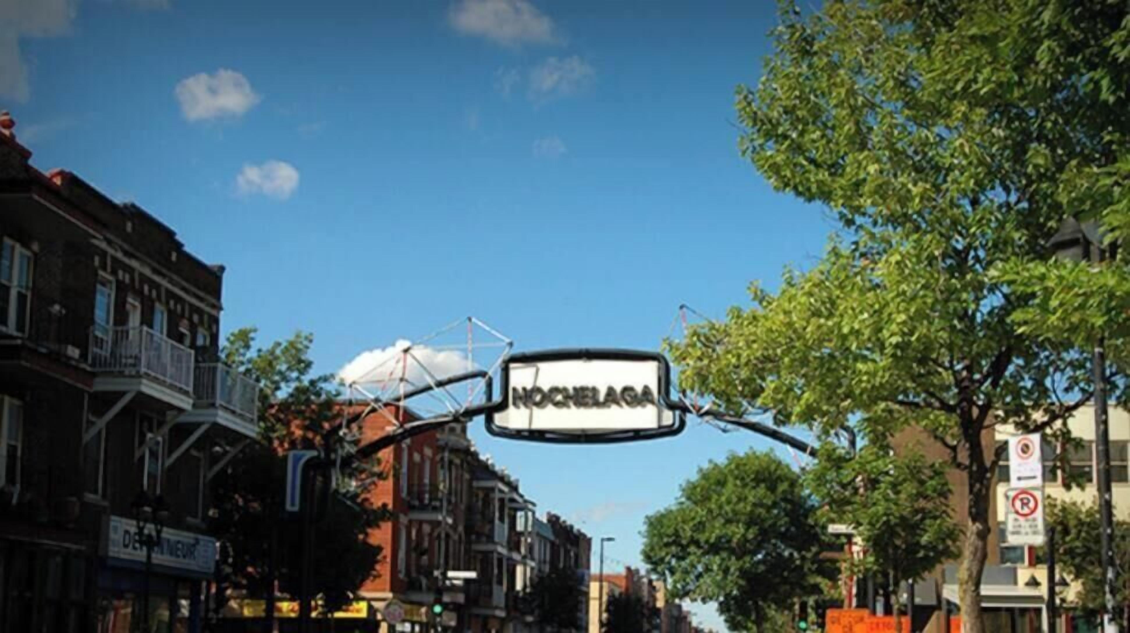 A street view with a sign reading "NOCHELAAG" and various buildings along the street.