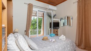 Ein Schlafzimmer mit Bett, Kleiderschrank, Spiegel und einem Balkon mit Vorhängen.