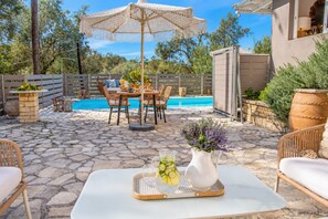 An outdoor patio with stone flooring, a pool, wicker furniture, and a white table with a vase. - Dimitris Cottage - Two Bedroom Villa, Sleeps 4 (Apergatika)