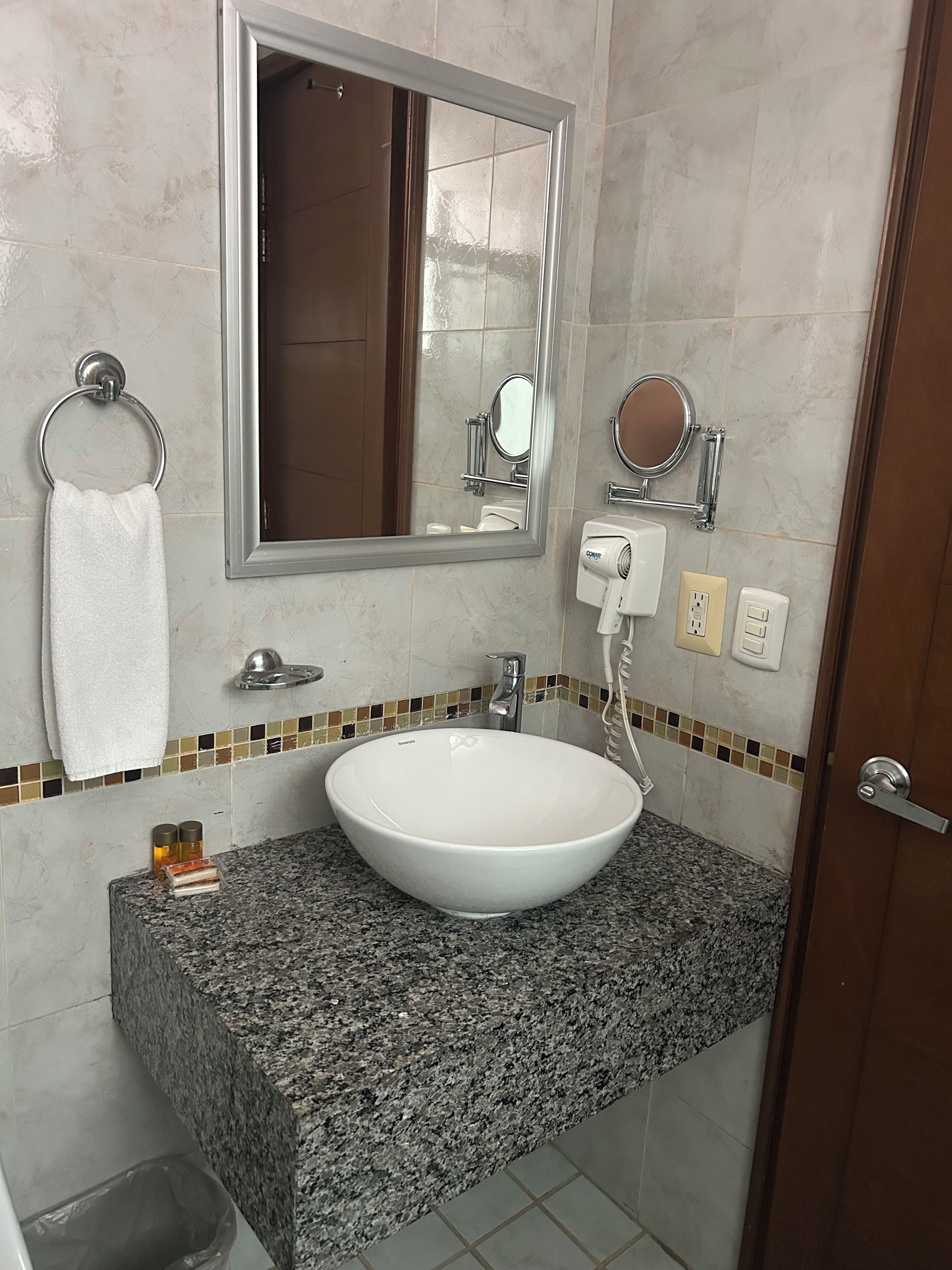 Un baño con lavamanos blanco, espejo, toallero, secador de mano y salpicadero de azulejos.