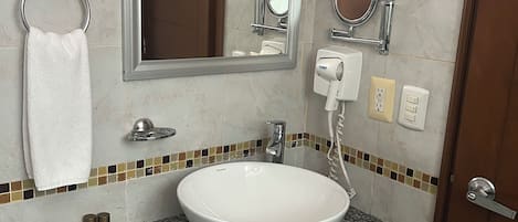 Un baño con lavamanos blanco, espejo, toallero, secador de mano y salpicadero de azulejos.