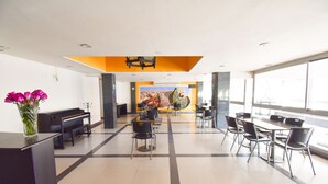 Eine geräumige Lobby mit Klavier, Wandgemälde und einer Sitzecke mit Tischen und Stühlen.
