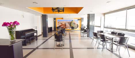 A spacious lobby with a piano, a mural, and a seating area with tables and chairs.