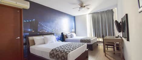 Habitación de hotel con dos camas, un escritorio, un ventilador de techo y un mural con vista a la ciudad.