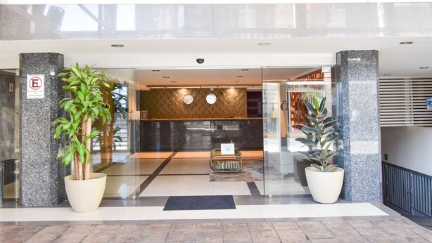 Eine moderne Hotelhalle mit einer Rezeption, Topfpflanzen und einem Glastürbereich.