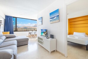 Moderni hotellihuone, jossa on suuri ikkuna, taulutelevisio, sohva, sänky ja pieni ruokailutila.