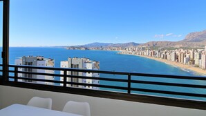 Een hotelkamer met een balkon dat uitkijkt over een kuststadsgezicht, met uitzicht op zee en bergen.